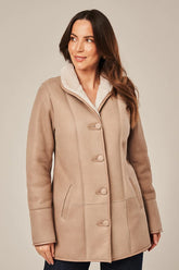 Woman wearing a beige coat with a white collar against a plain background