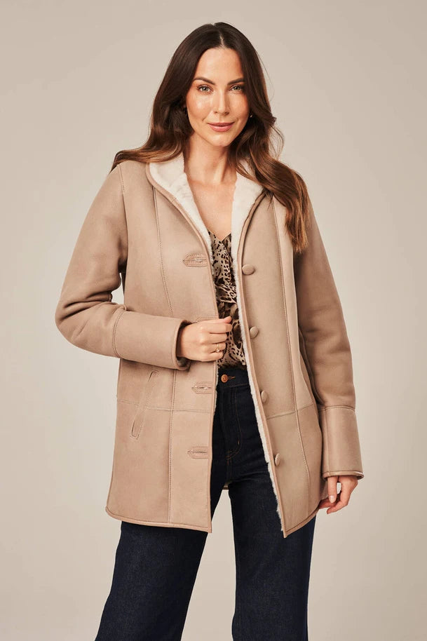Woman wearing a beige coat with a white collar against a plain background