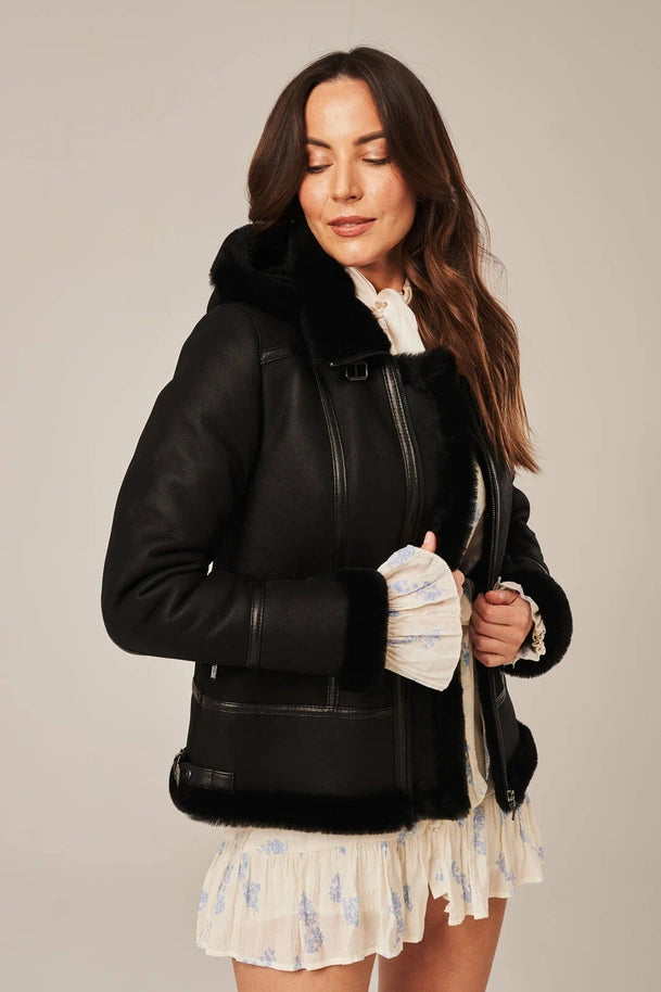 Woman wearing a black leather jacket with fur trim on a plain background