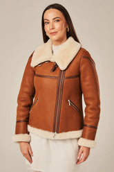 Woman wearing a brown leather jacket with white fur lining on a beige background