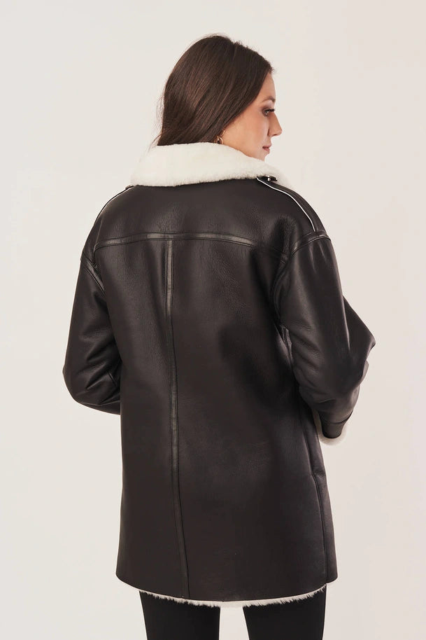 Woman wearing a black leather jacket with white fur trim on a plain background
