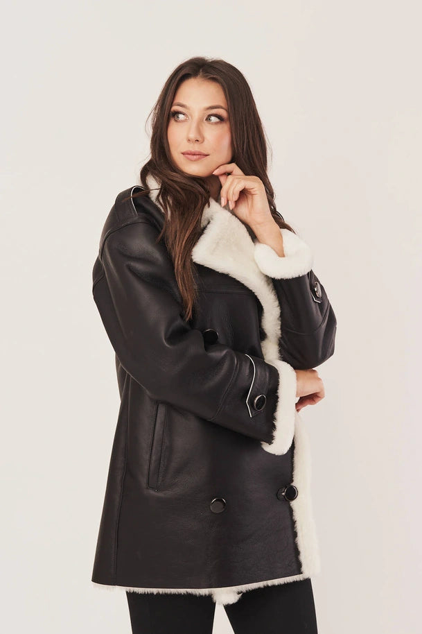 Woman wearing a black leather coat with white fur trim on a light background