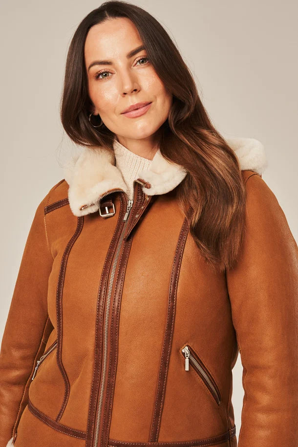 Woman wearing a brown leather jacket with fur trim on a plain background