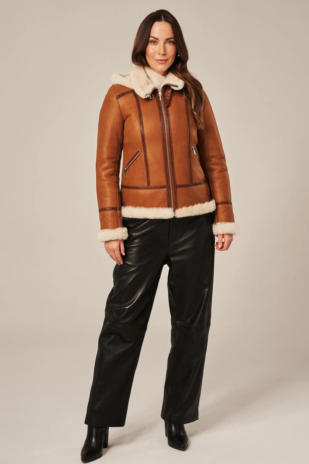 Woman wearing a brown leather jacket with white fur trim and black pants on a beige background