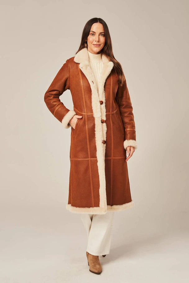 Woman wearing a brown shearling coat with white fur lining on a plain background