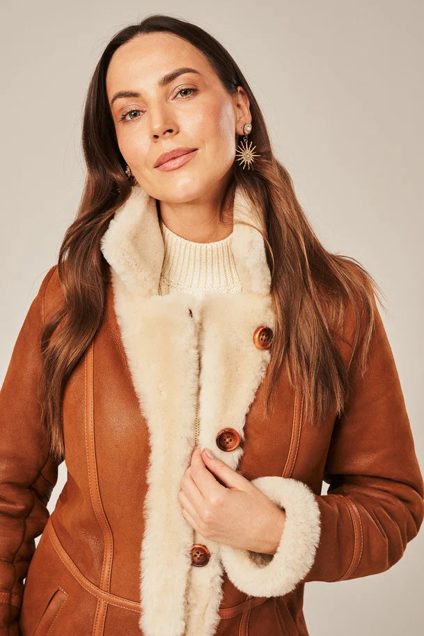 Woman wearing a brown leather coat with white fur lining against a neutral background