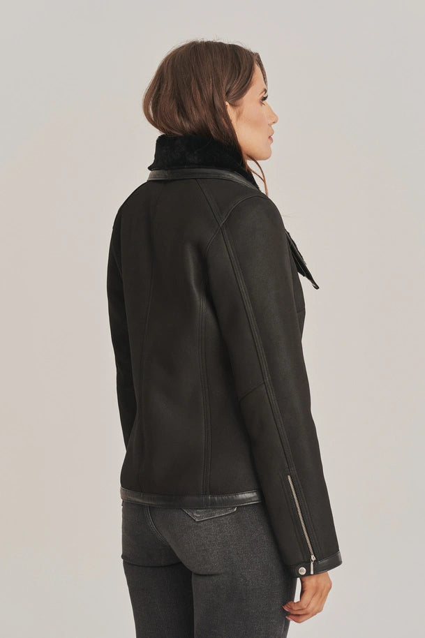 Person wearing a black leather jacket with fur collar on a plain background